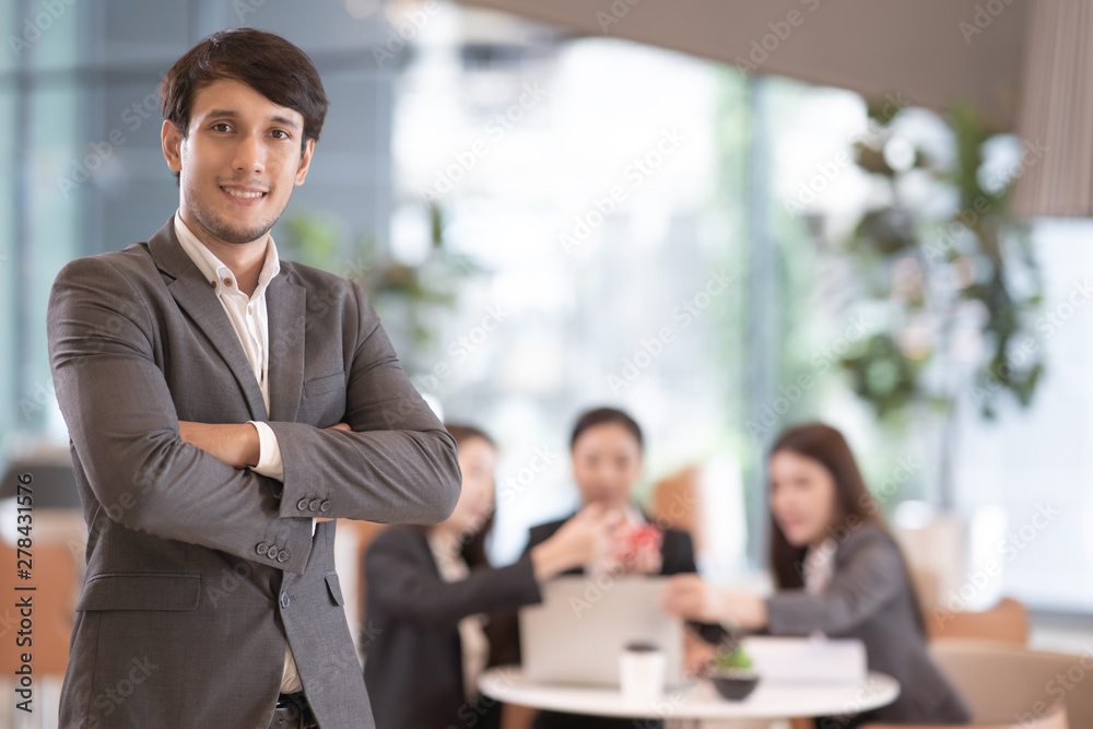 Portrait of successful young Asian businessmanÂ at office, colleagues in background. - obrazy, fototapety, plakaty 