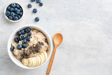 Wall Mural - Healthy Breakfast Oatmeal Bowl With Banana, Blueberry And Chia Seeds In Bowl On Grey Concrete Background. Top View Copy Space