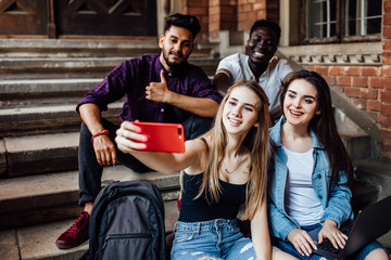 Wall Mural - Young blonde woman making selfie with her friends students, while they are sitting on stairs.