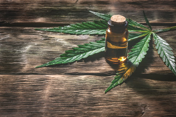 Cannabis essential oil in the vial with a green leaf on a wooden table background with a copy space. Herbal medicine concept.