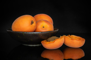 Group of three whole two halves of fresh deep orange apricot on grey ceramic plate with a stone isolated on black glass