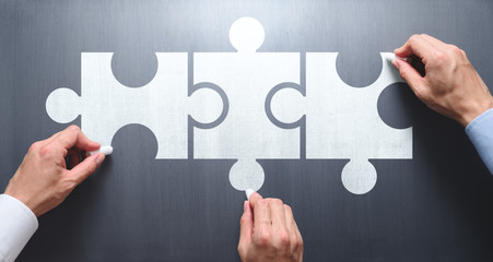Poster - Finding solution of business relationship. Successful business team concept. Businessmen drawing puzzle pieces on chalkboard.