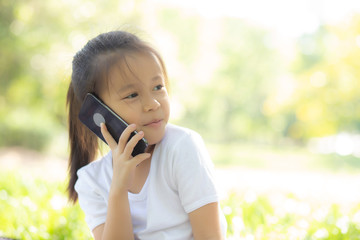 Beautiful portrait asian child happy and talking smart mobile phone in the nature park in summer, asia kid cellphone, little girl casual relax and leisure, communication concept.