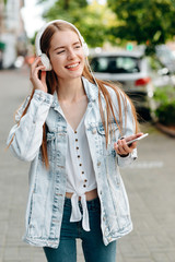 Happy girl holding a smartphone and listening music in an earphones outdoor- Image