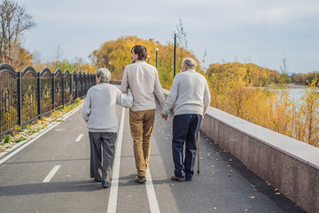 An elderly couple walks in the park with a male assistant or adult grandson. Caring for the elderly, volunteering