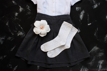 White shirt, grey skirt and stationery supplies on black background. The first of september, new school year.