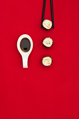 Wall Mural - Fresh sushi rolls; soya sauce in spoon and black chopsticks on dark red surface