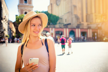 Europe travel summer tourism holiday vacation background - young attractive Caucasian smiling beautiful blonde girl face with hat mobile cell phone and using backpack in hand having chat in city