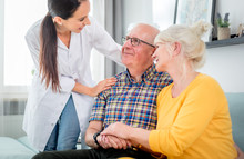 Smiling Nurse Talking With Senior Couple During Home Visit