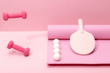 Wall Mural - pink dumbbells levitating in air near white ping-pong balls and racket on fitness mat on pink background