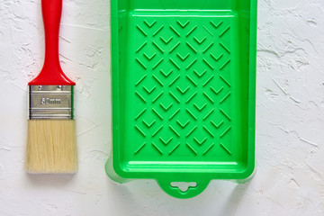 brush with red handle and green paint tray on white concrete background. tools and accessories for home renovation. Top view