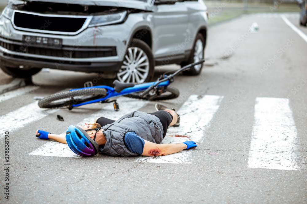 Scene of a road accident with injured cyclist lying on the pedestrian crossing near the broken bicycle and car - obrazy, fototapety, plakaty 