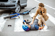 © rh2010 - Road accident with injured cyclist lying on the pedestrian crossing near the broken bicycle, worried woman driver calling and checking men's pulse