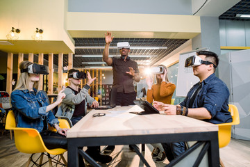 Group of friends and their African man couch trying vr glasses while sitting at the table in office. virtual reality with people having fun together with wearable headset googles