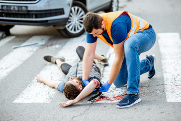 Wall Mural - Man applying first aid to the injured bleeding person, wearing tourniquet on the arm after the road accident on the pedestrian crossing