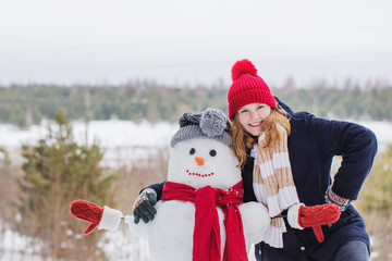 happy teenager girl with snowman in winter forest