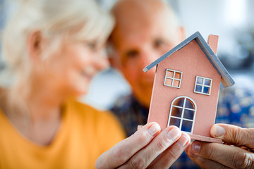 New house concept, happy senior couple holding small home model