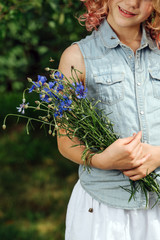 Teenage girl with curly hair is holding blue bouquet of meadow flowers