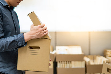 Wall Mural - Young Asian man opening cardboard box lid near product shelves in warehouse. Parcel shipping service and delivery packaging. Unboxing or unpacking concepts