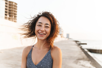 Sticker - Portrait closeup of beautiful woman smiling and looking at camera while walking by seaside in morning