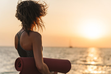 Poster - Photo from back of caucasian sportswoman looking away while standing with yoga mat by seaside in morning