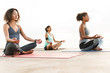 Photo of relaxed multiethnic sportswomen meditating and doing zen gestures while sitting on yoga mats by seaside in morning