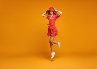 concept happy emotional young woman in red summer dress and hat jumping   on yellow background