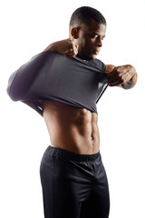 serious young sexy man takes off his black t-shirt, isolated on white, guy showing his stomach in the sport studio.close up side view photo. preparation for taking a shower