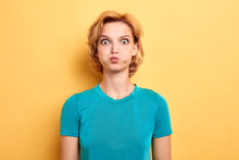Annoyed Irritated Young Woman In Blue T-shirt Blowing Her Cheeks, Frowning, Feeling Frustrated With Something. Isolated Yellow Background