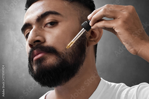 Fotomural Bearded man holding pippete with beard oil...