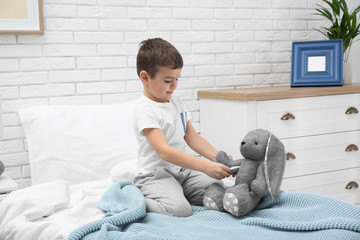 Wall Mural - Cute child playing doctor with stuffed toy on bed in hospital ward