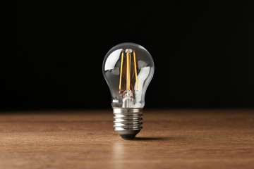 Wall Mural - Vintage filament lamp bulb on wooden table against black background