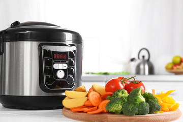 Poster - Modern multi cooker and wooden board with vegetables on white table in kitchen