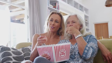 Wall Mural - Mother With Adult Daughter Eating Popcorn Watching Movie On Sofa At Home Together