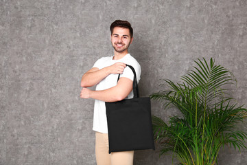 Canvas Print - Portrait of young man with eco bag at indoor palm plant near grey wall