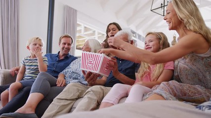 Wall Mural - Multi-Generation Family Sitting On Sofa At Home Eating Popcorn And Watching Movie Together