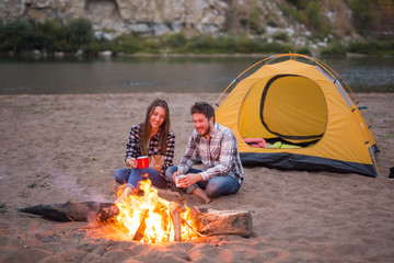 People, tourism and nature concept - Man embrace woman sitting near a fire