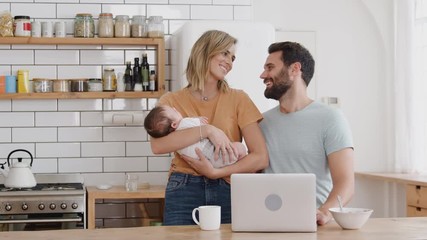 Wall Mural - Portrait Of Family In Kitchen At Breakfast With Mother Caring For Baby Son And Father Using Laptop