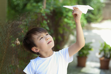 Happy cute Asian child boy playing with paper airplane outdoors