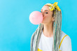 girl with dreadlocks and headband blowing bubblegum isolated on turquoise