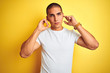 © Krakenimages.com - Young caucasian man wearing casual white t-shirt over yellow isolated background covering ears with fingers with annoyed expression for the noise of loud music. Deaf concept.