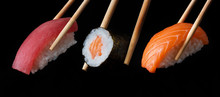 Traditional Japanese Sushi Pieces Placed Between Chopsticks, Separated On Black Background