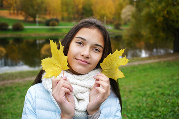 beautiful teen girl holding two yellow autumn leaves in her hands, close-up portrait