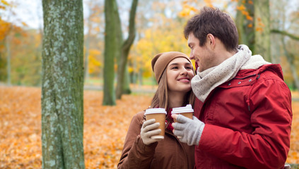 Wall Mural - love, relationships, season and people concept - happy young couple with coffee cups walking in autumn park