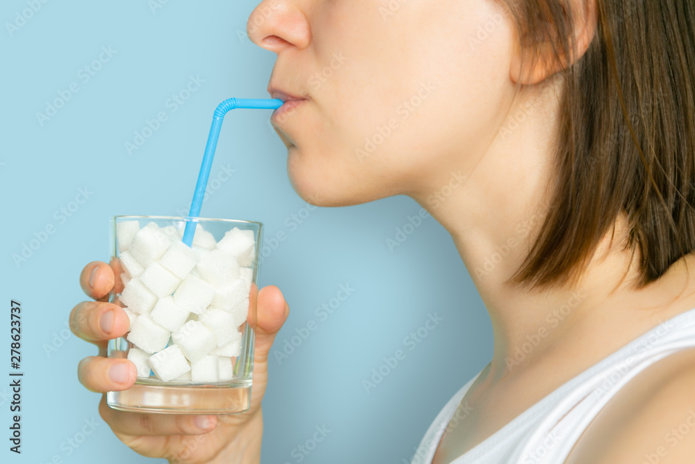 Excessive sugar consumption concept - female drinking from glass with sugar cubes, blue background - obrazy, fototapety, plakaty 