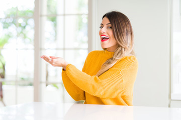 Wall Mural - Young beautiful woman wearing winter sweater at home Pointing to the side with hand and open palm, presenting ad smiling happy and confident