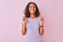 Young Brazilian Woman Wearing T-shirt Standing Over Isolated Pink Background Gesturing Finger Crossed Smiling With Hope And Eyes Closed. Luck And Superstitious Concept.