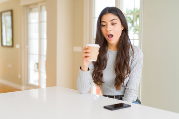 Poster - Young woman drinking a cup of coffee at home scared in shock with a surprise face, afraid and excited with fear expression