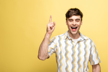 cheerful young man showing idea sign while smiling at camera on yellow background