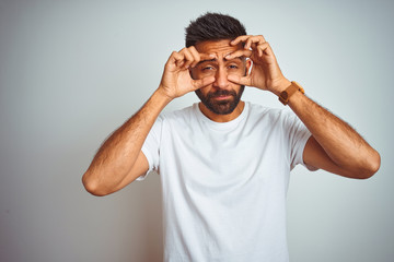 Wall Mural - Young indian man wearing t-shirt standing over isolated white background Trying to open eyes with fingers, sleepy and tired for morning fatigue